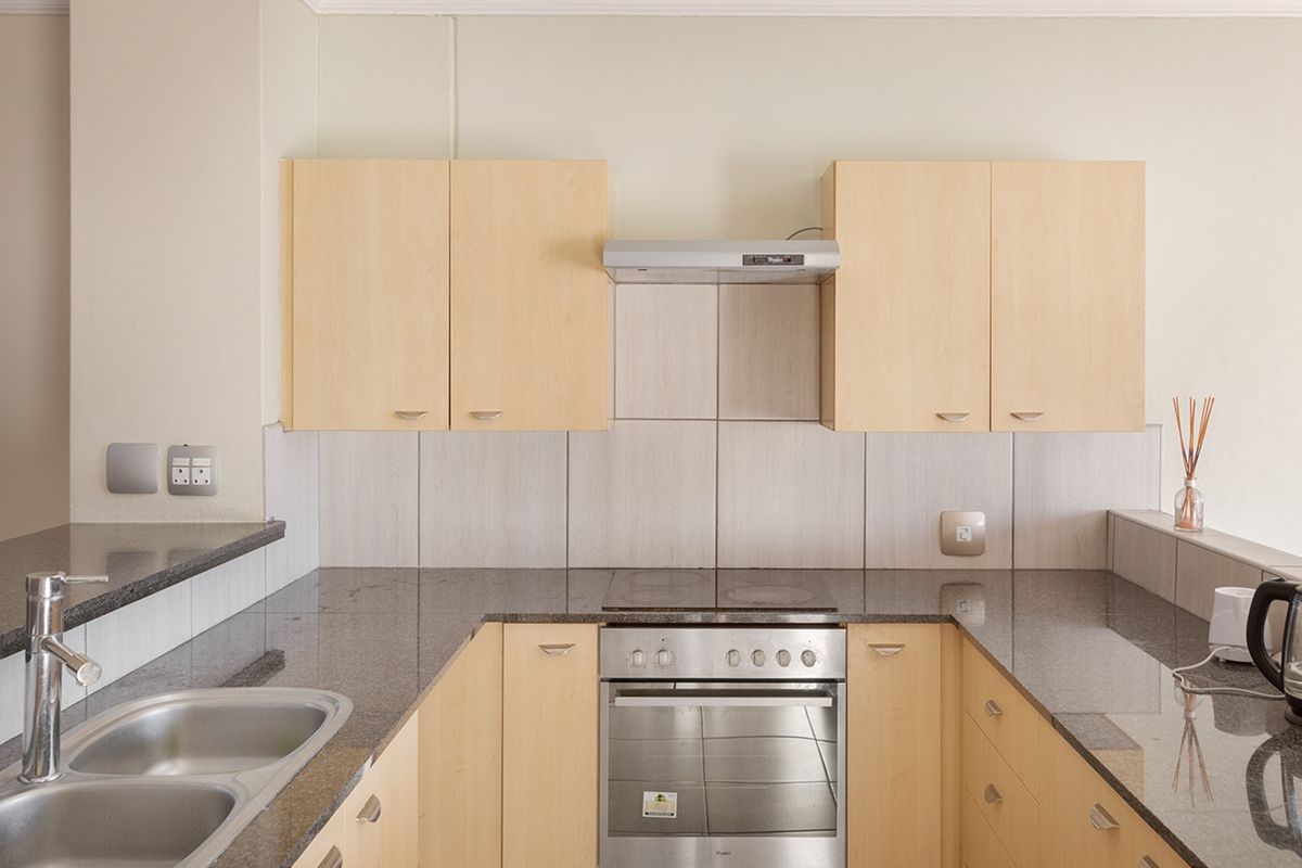 A functional kitchen featuring light wood cabinetry, granite countertops, a stainless steel sink, and integrated cooking appliances with a tiled backsplash.