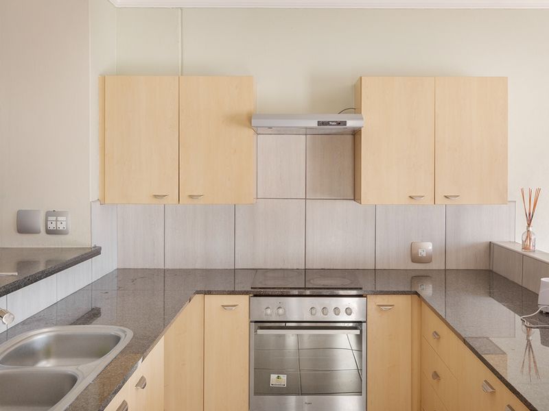 A functional kitchen featuring light wood cabinetry, granite countertops, a stainless steel sink, and integrated cooking appliances with a tiled backsplash.
