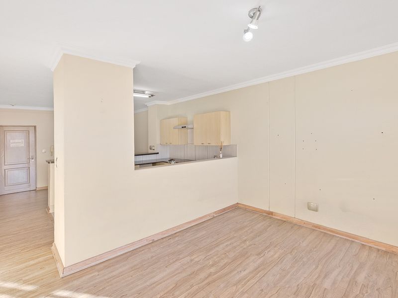 An empty open-plan living and kitchen area featuring laminate flooring, neutral walls, and built-in kitchen cabinetry with an extractor fan.