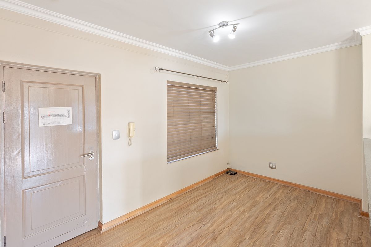 An empty bedroom featuring laminate flooring, neutral walls, cove cornicing, and a fitted intercom system with venetian blinds.