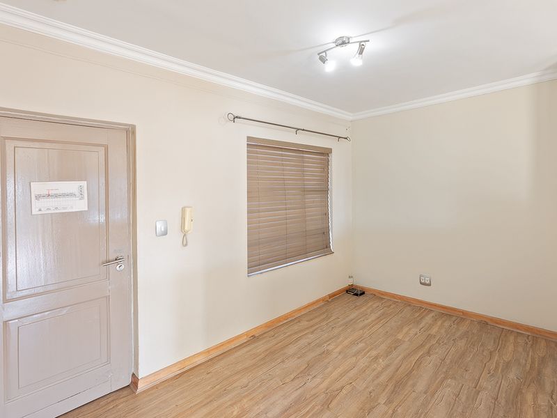 An empty bedroom featuring laminate flooring, neutral walls, cove cornicing, and a fitted intercom system with venetian blinds.