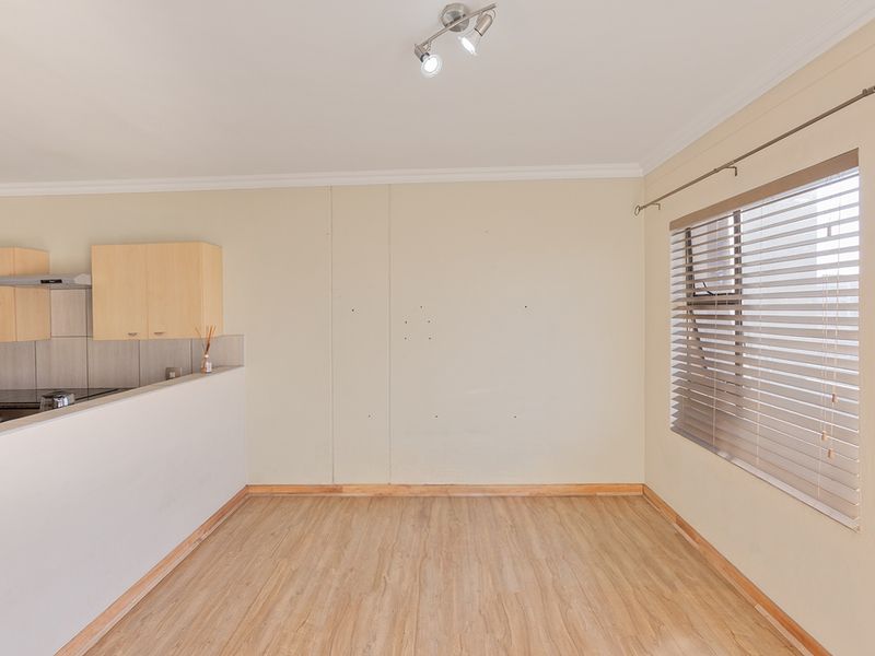 An open-plan living and kitchen area featuring laminate flooring, neutral walls, and built-in kitchen cabinetry with an extractor fan.