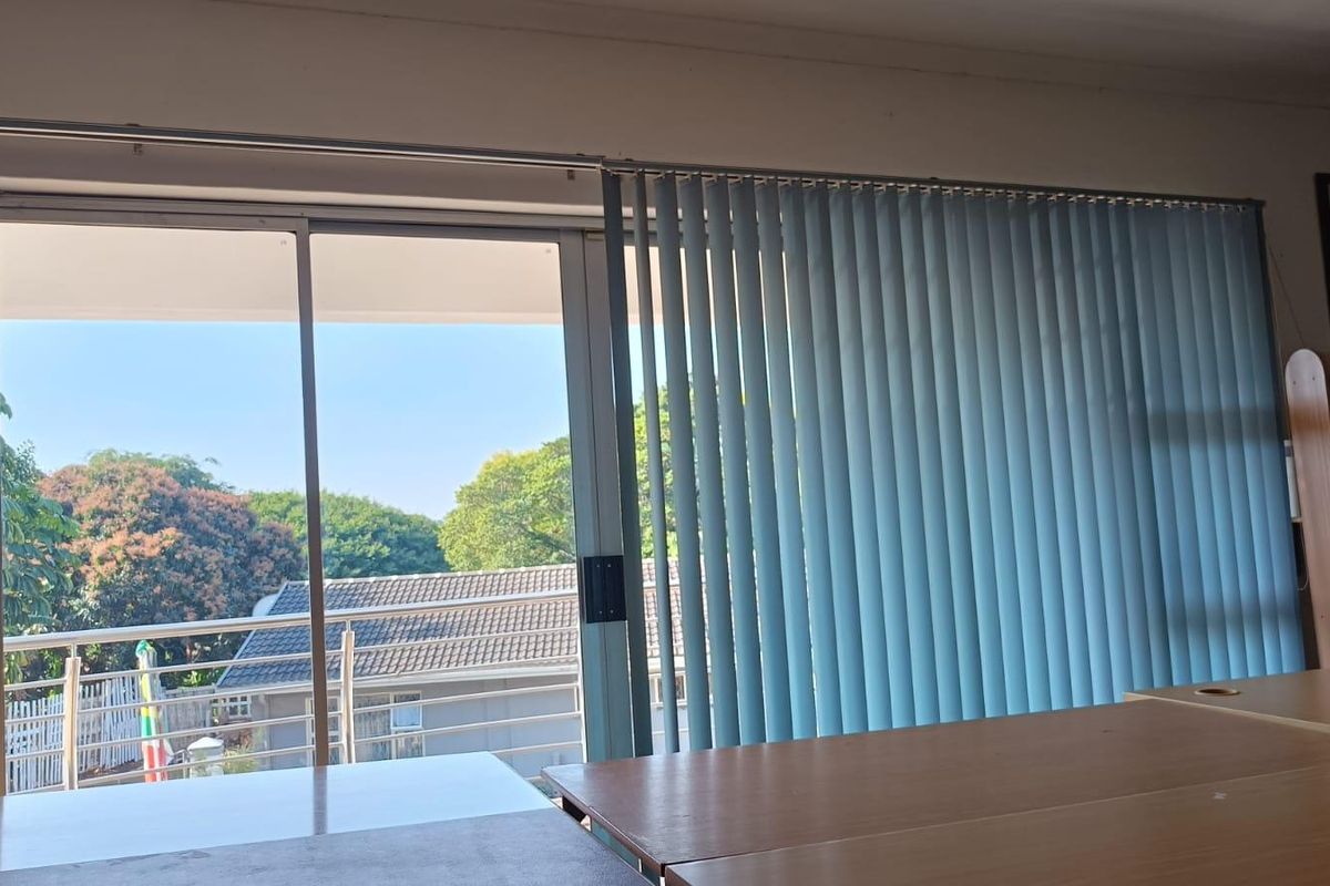 Living area featuring a large sliding glass door with vertical blinds, providing direct access to an outdoor balcony with neighborhood views.