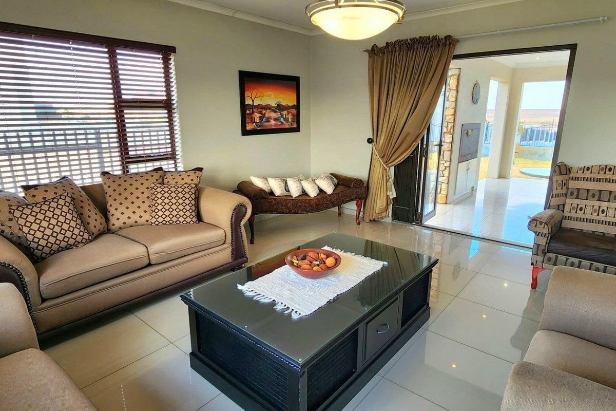 Spacious living room featuring polished tile flooring, large windows with venetian blinds, and direct access to an outdoor patio area.