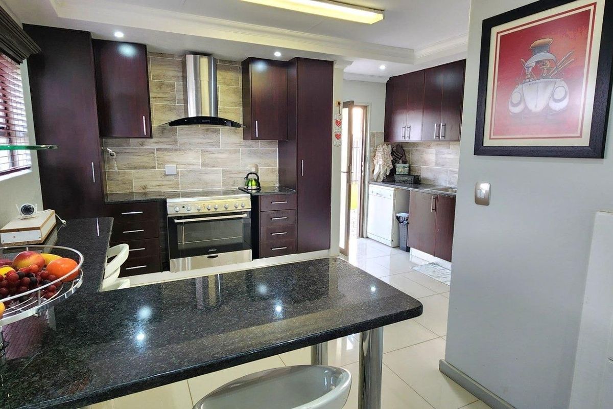 Modern kitchen featuring dark wood cabinetry, granite countertops, a breakfast bar, and stainless steel appliances with a tiled backsplash.