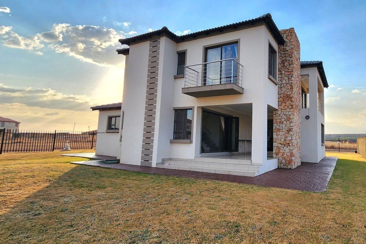 Rear view of a modern two-story house featuring stone cladding, a private balcony, and a covered patio area overlooking the garden.