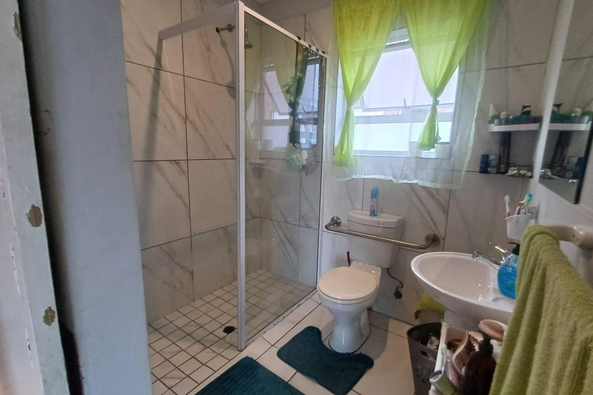 A functional bathroom featuring a walk-in shower with glass enclosure, pedestal basin, and toilet, finished with marble-look wall tiles.