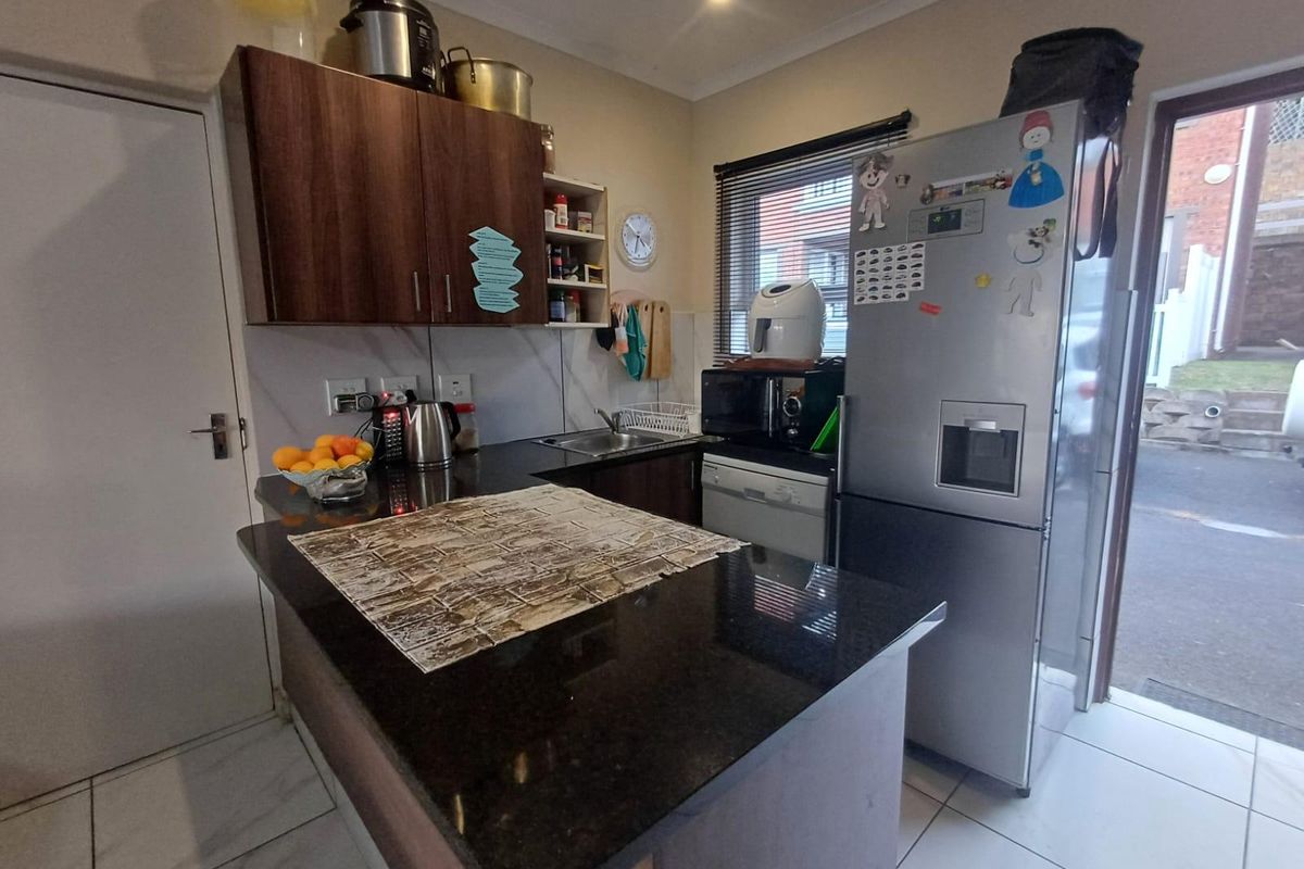 Compact kitchen featuring dark granite countertops, laminate cabinetry, tiled flooring, and direct access to the exterior.