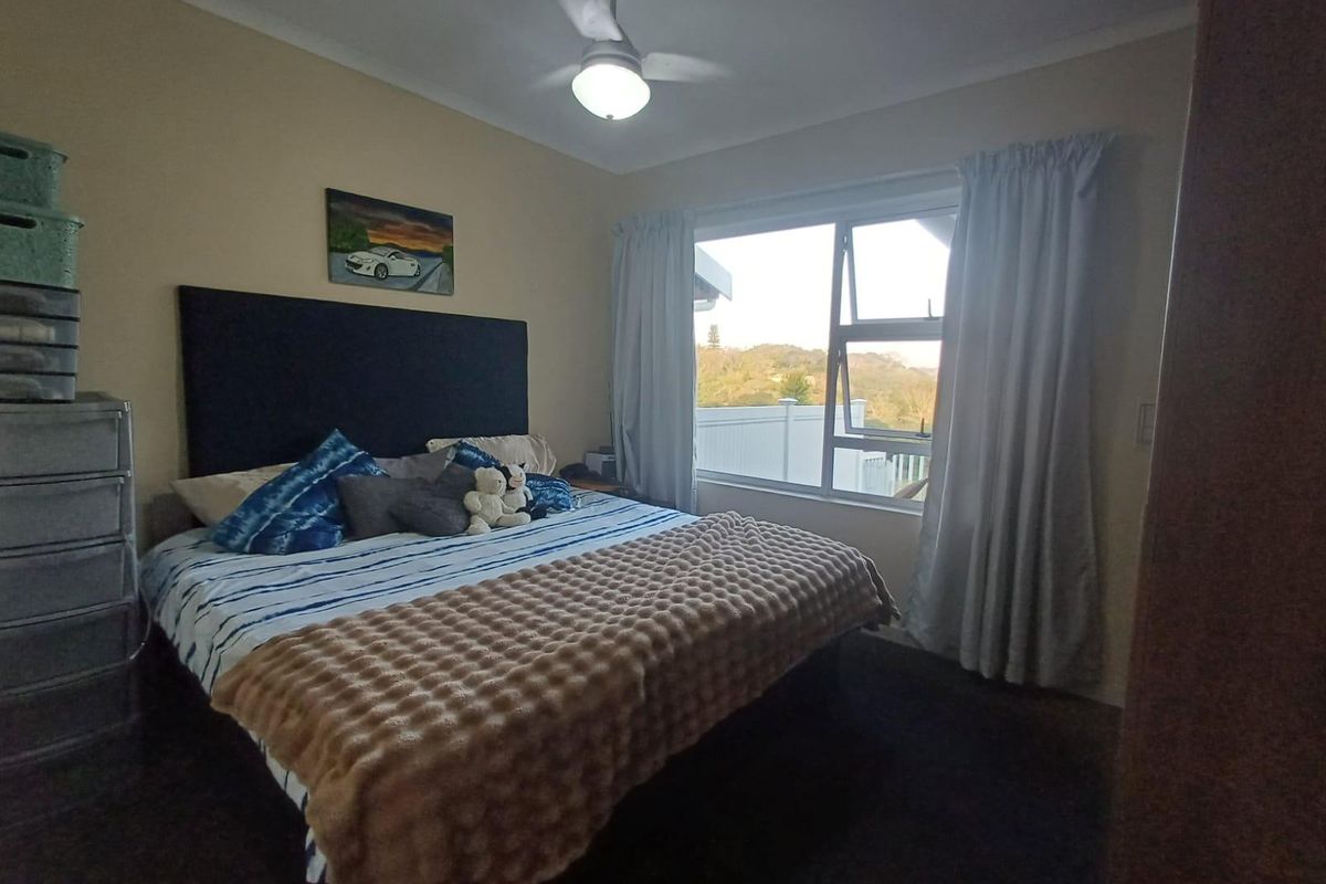 A functional bedroom featuring a ceiling fan, aluminium window frame, and built-in storage, offering a comfortable space with natural light.