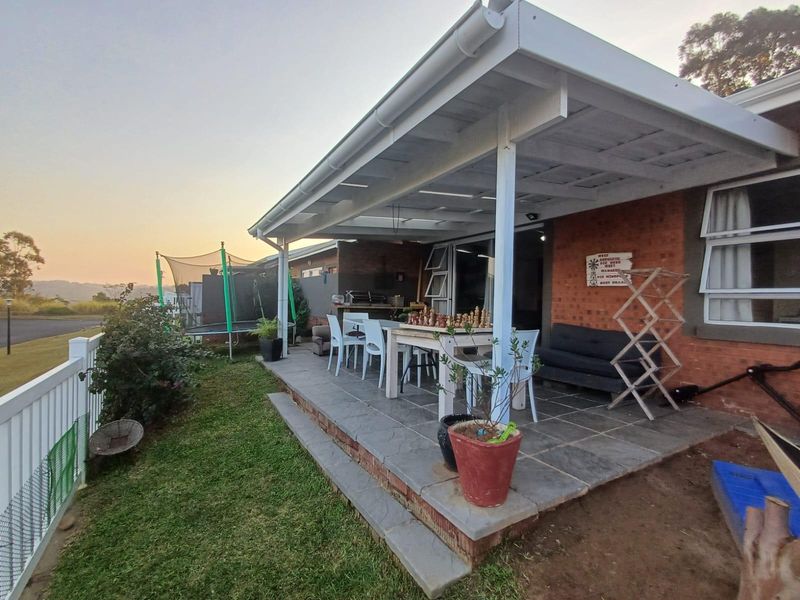 A covered outdoor patio featuring stone tile flooring and a built-in braai, providing a functional space for outdoor entertaining and relaxation.