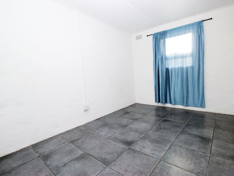 A vacant bedroom featuring dark tiled flooring and white walls, providing a blank canvas for potential interior design and furnishing.