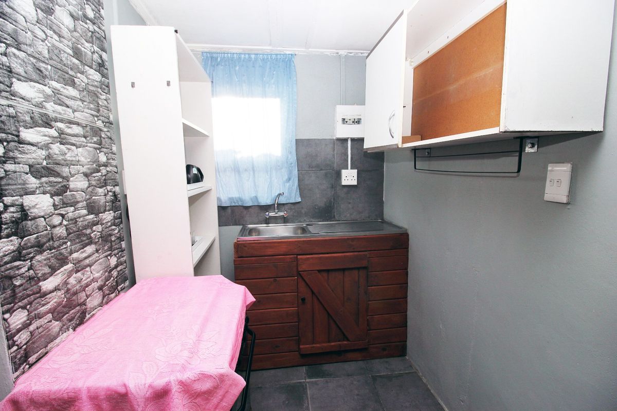 A compact scullery or utility area featuring a stainless steel sink, tiled splashback, and basic built-in cabinetry with some unfinished elements.