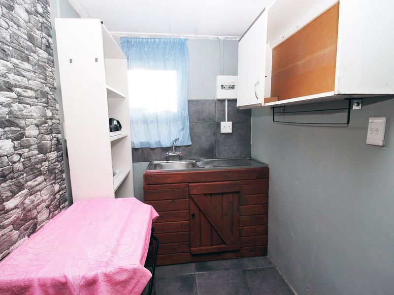 A compact scullery or utility area featuring a stainless steel sink, tiled splashback, and basic built-in cabinetry with some unfinished elements.