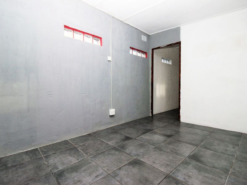 An empty room featuring dark tiled flooring, grey and white painted walls, and high-set clerestory windows.