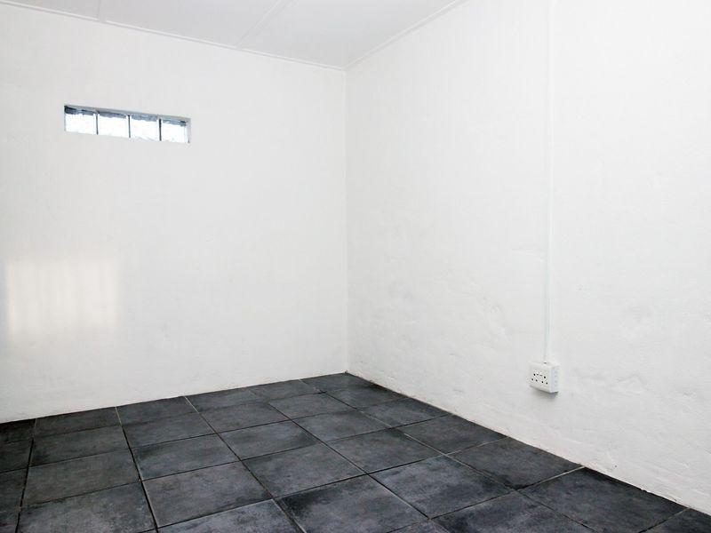 An empty, neutral-toned room featuring dark tiled flooring and a high-level clerestory window, providing a blank canvas for potential bedroom or office use.