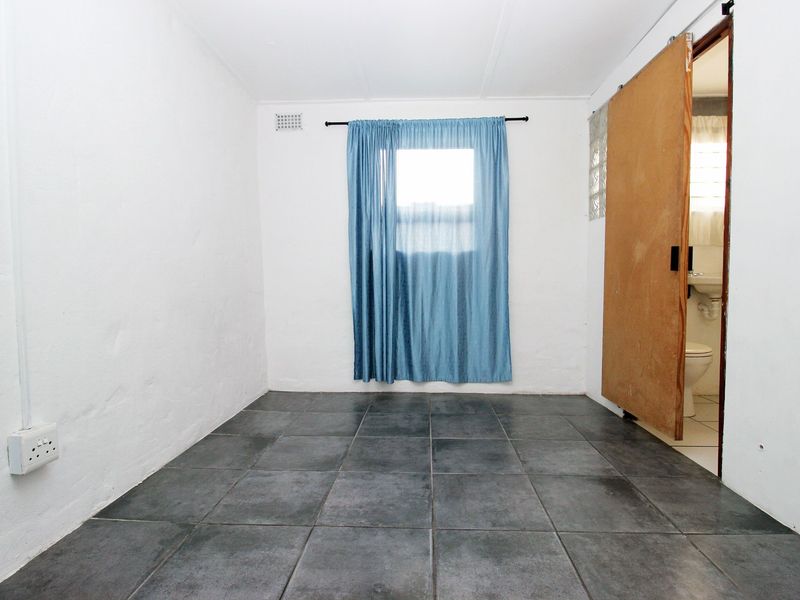 An empty bedroom featuring dark tiled flooring, a sliding door leading to an en-suite bathroom, and a window with blue curtains.