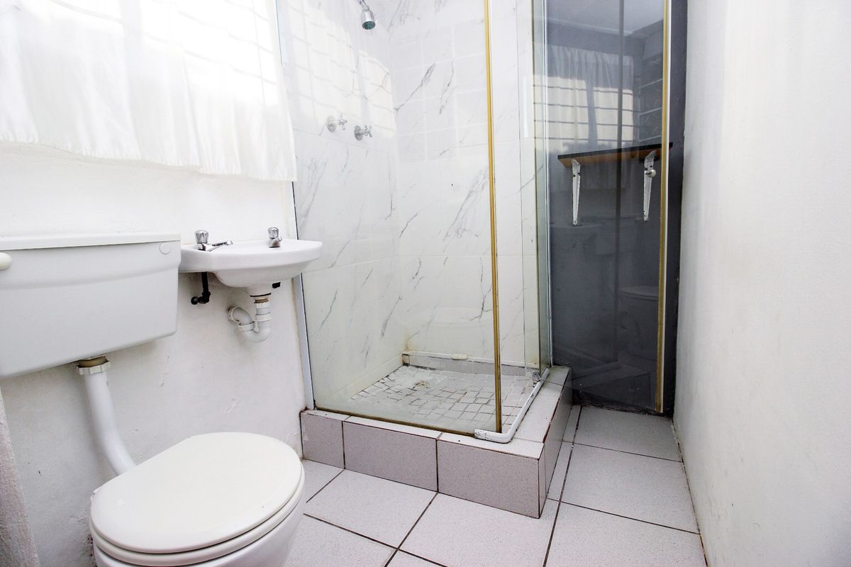 A compact bathroom featuring a shower enclosure, wall-mounted basin, and toilet with tiled finishes throughout.