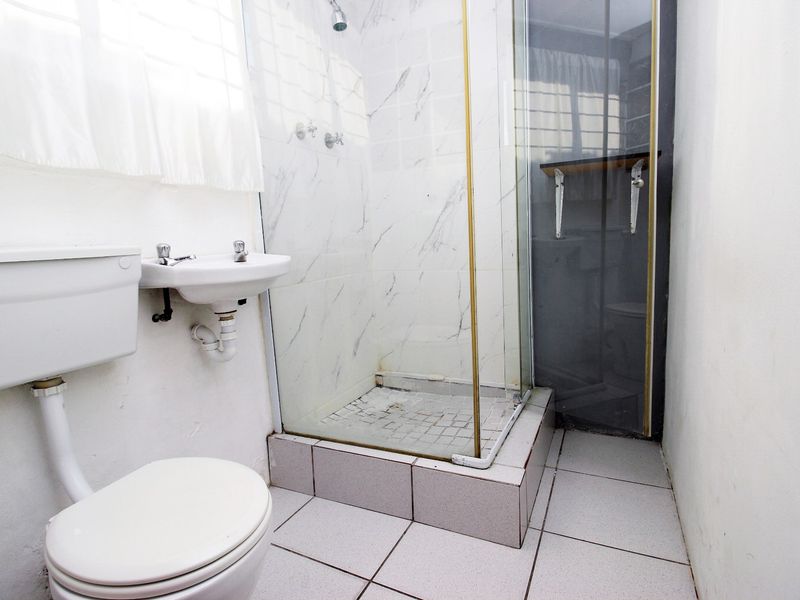 A compact bathroom featuring a shower enclosure, wall-mounted basin, and toilet with tiled finishes throughout.