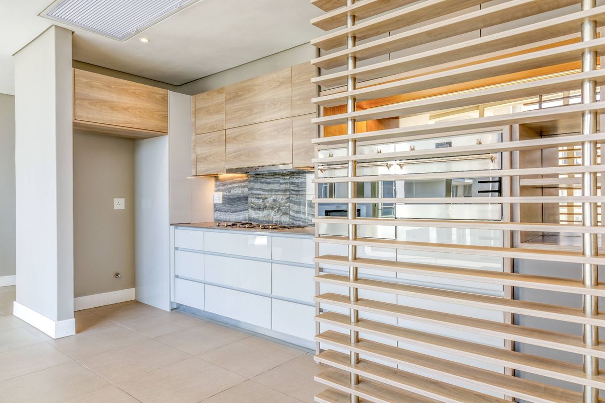 Modern kitchen featuring light wood cabinetry, stone splashback, integrated appliances, and a decorative timber slat screen divider in an open-plan layout.