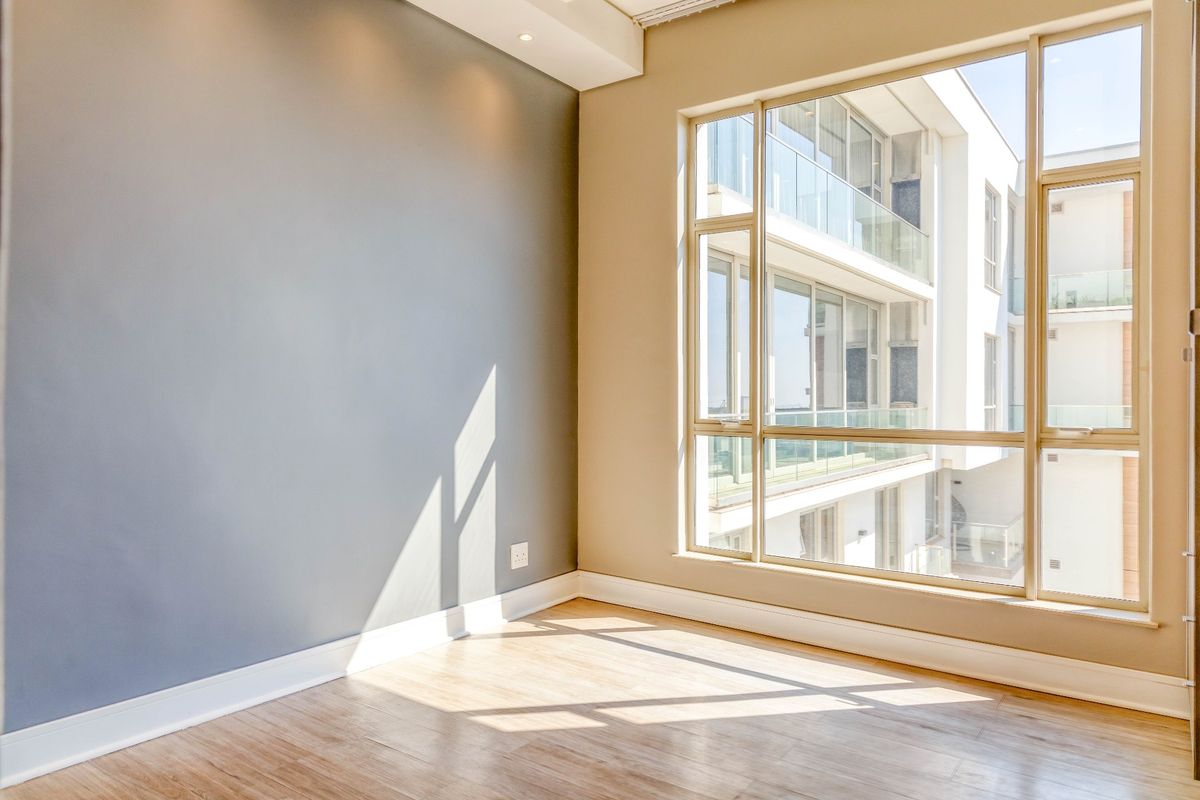 A bright, empty bedroom featuring large floor-to-ceiling windows, modern laminate flooring, and recessed ceiling lighting, offering a clean and neutral living space.