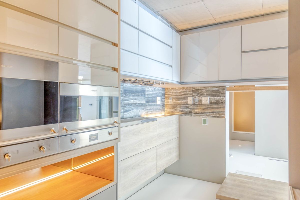 Modern kitchen featuring high-gloss cabinetry, built-in stainless steel appliances, and elegant stone tile backsplash with integrated under-cabinet lighting.