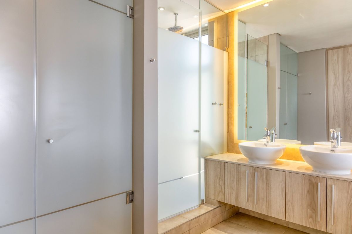 Modern bathroom featuring a double vanity with vessel sinks, backlit mirror, and a spacious walk-in shower with a frosted glass enclosure.