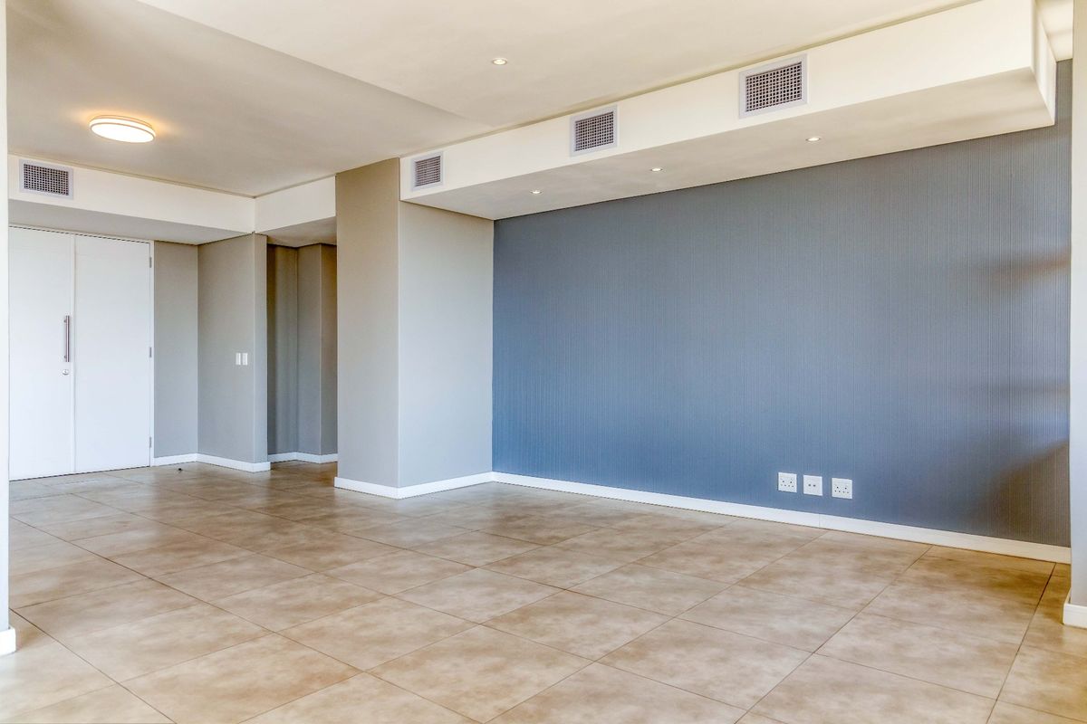 A spacious, empty living area featuring neutral tiled flooring, a blue feature wall, and integrated ducted air conditioning vents.