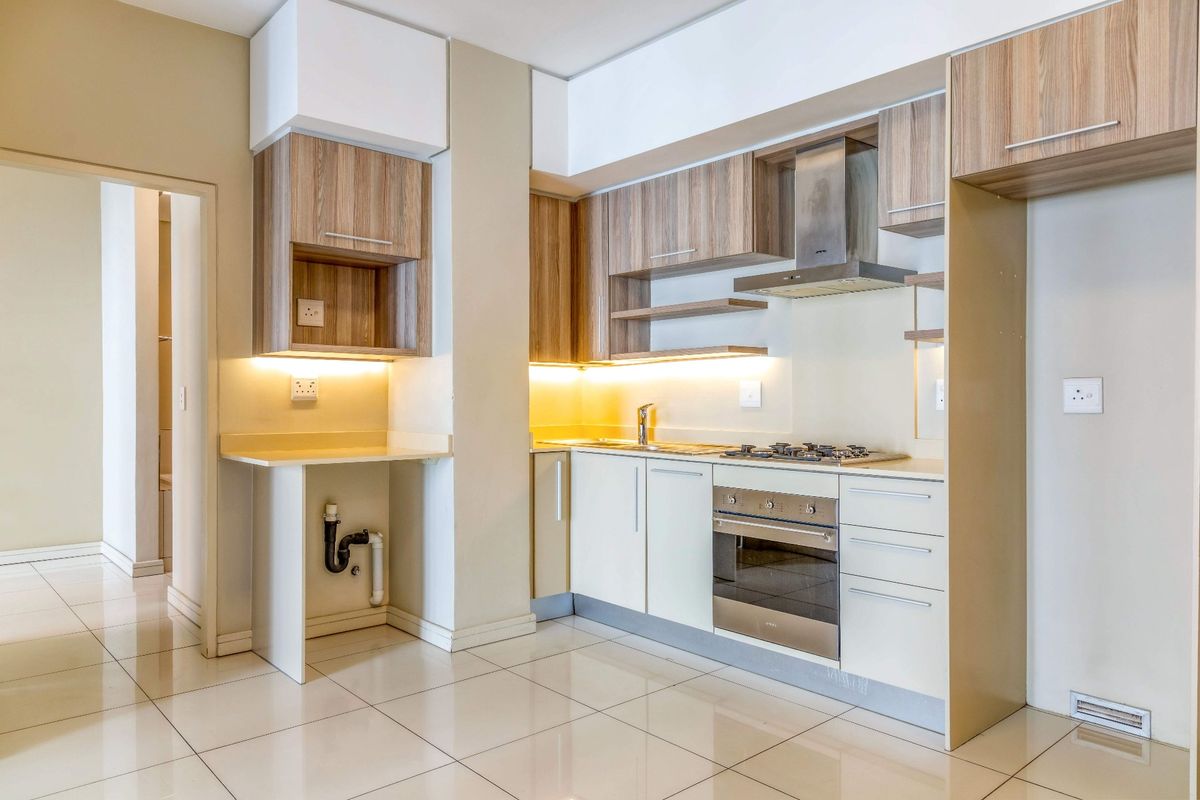 Modern kitchen featuring light wood-tone cabinetry, stainless steel oven, gas hob, extractor fan, and tiled flooring with integrated under-cabinet lighting.