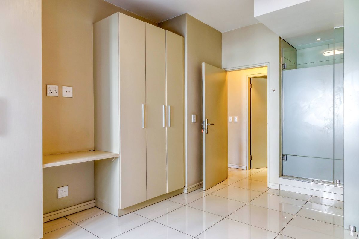 A clean, modern bedroom featuring built-in cabinetry, a integrated desk area, and direct access to an en-suite bathroom with a glass shower enclosure.