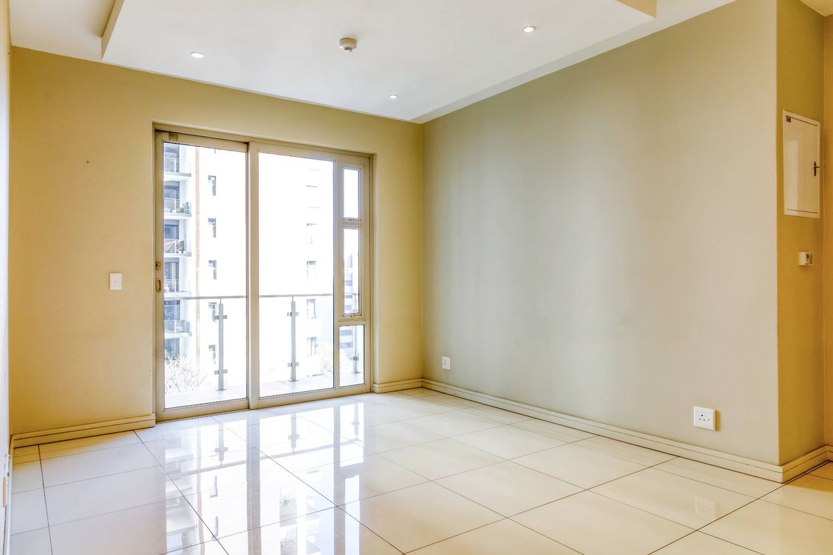 A bright, empty living area featuring polished tiled floors, recessed ceiling lights, and a large sliding glass door leading to a balcony.
