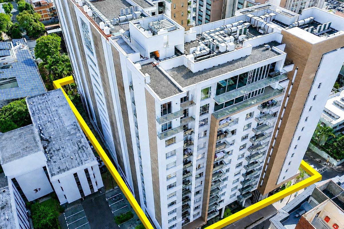 Aerial view of a modern multi-story apartment building featuring glass balconies and roof-mounted mechanical infrastructure.