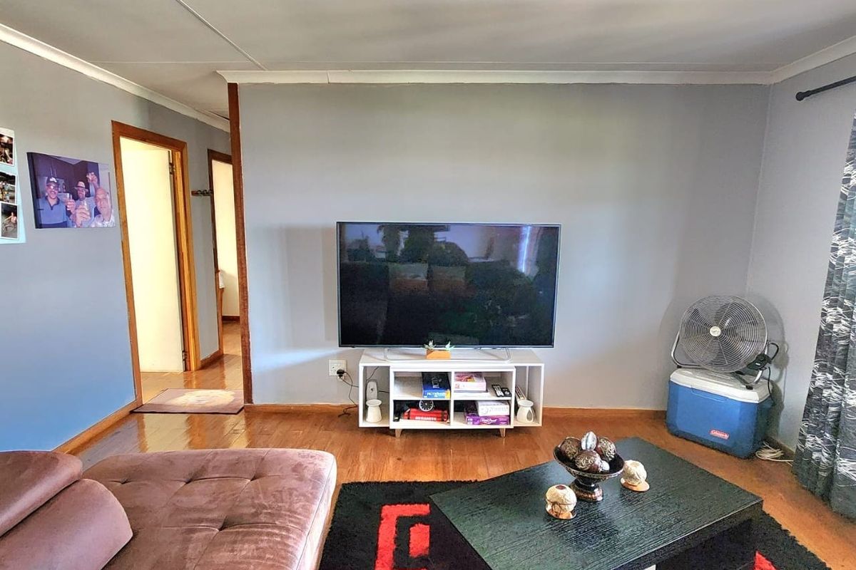 A living room featuring hardwood flooring and neutral wall tones, providing a functional space with access to adjacent hallways.
