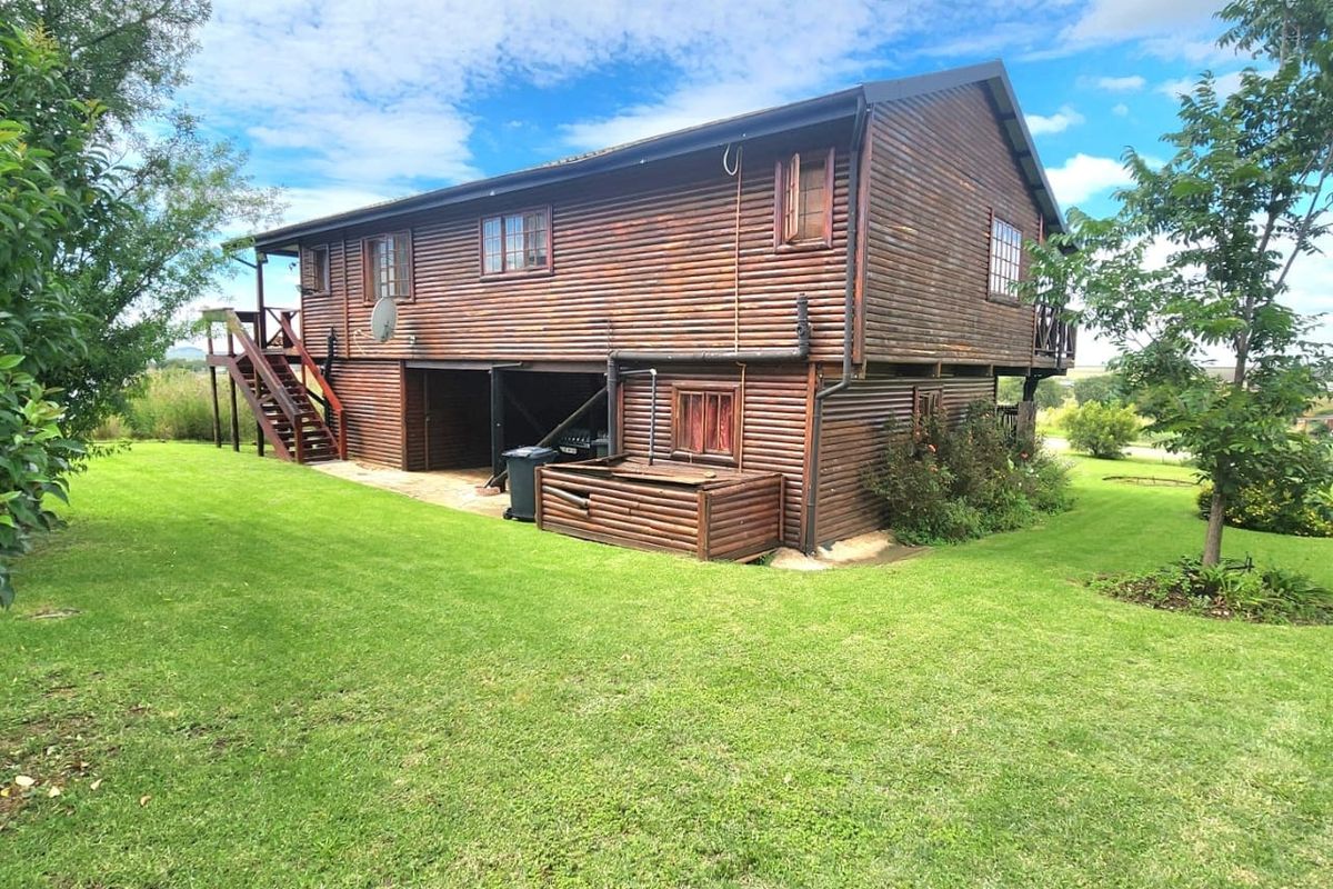 Rear view of a two-story timber log cabin featuring a raised deck, external staircase, and surrounding lawn area.