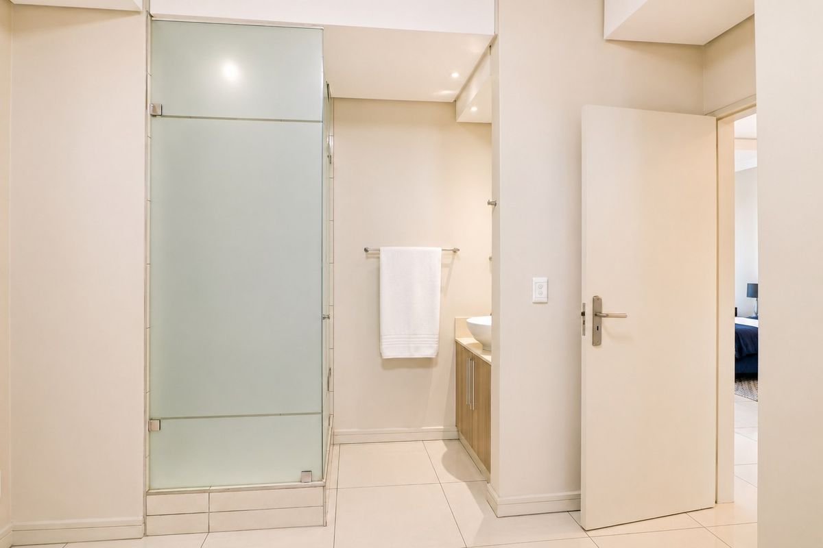 A clean, modern bathroom featuring a frosted glass shower enclosure, a vanity with a vessel sink, and neutral tiled flooring.