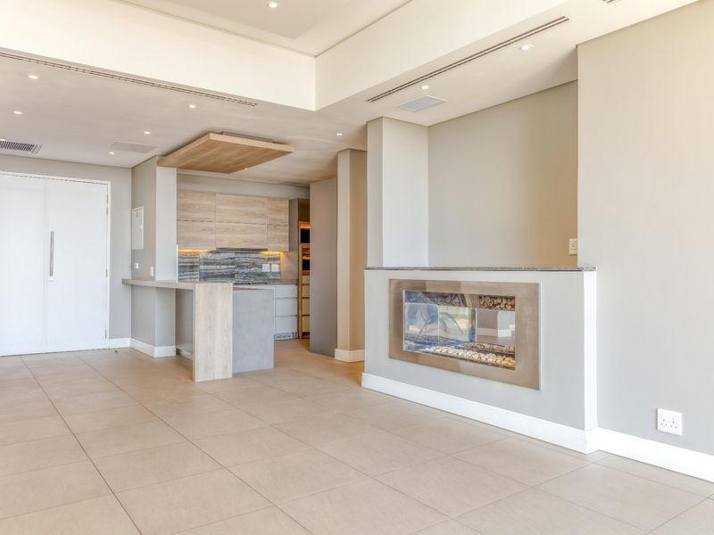 Spacious open-plan living area featuring a modern built-in fireplace, neutral tiled flooring, recessed lighting, and a sleek contemporary kitchen with integrated cabinetry.
