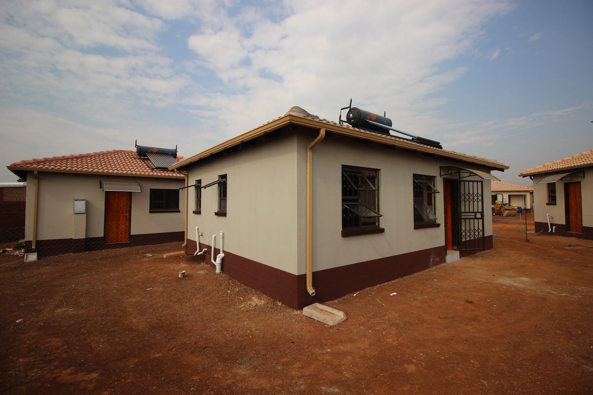 Rear view of a residential house featuring a solar water heating system, security bars on windows, and a security gate at the entrance.