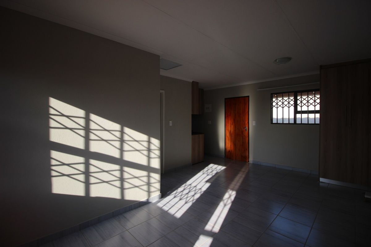 An empty bedroom featuring tiled flooring, built-in cupboards, and a security gate on the window, offering a clean and neutral living space.