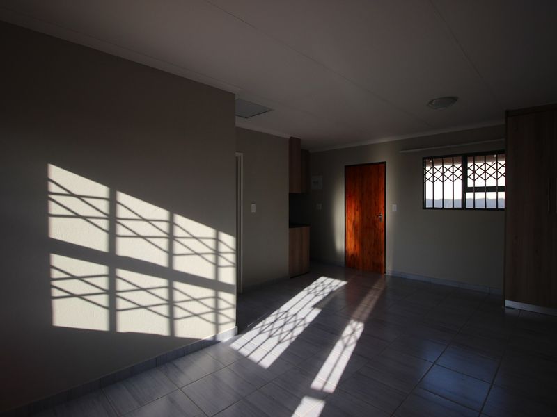 An empty bedroom featuring tiled flooring, built-in cupboards, and a security gate on the window, offering a clean and neutral living space.