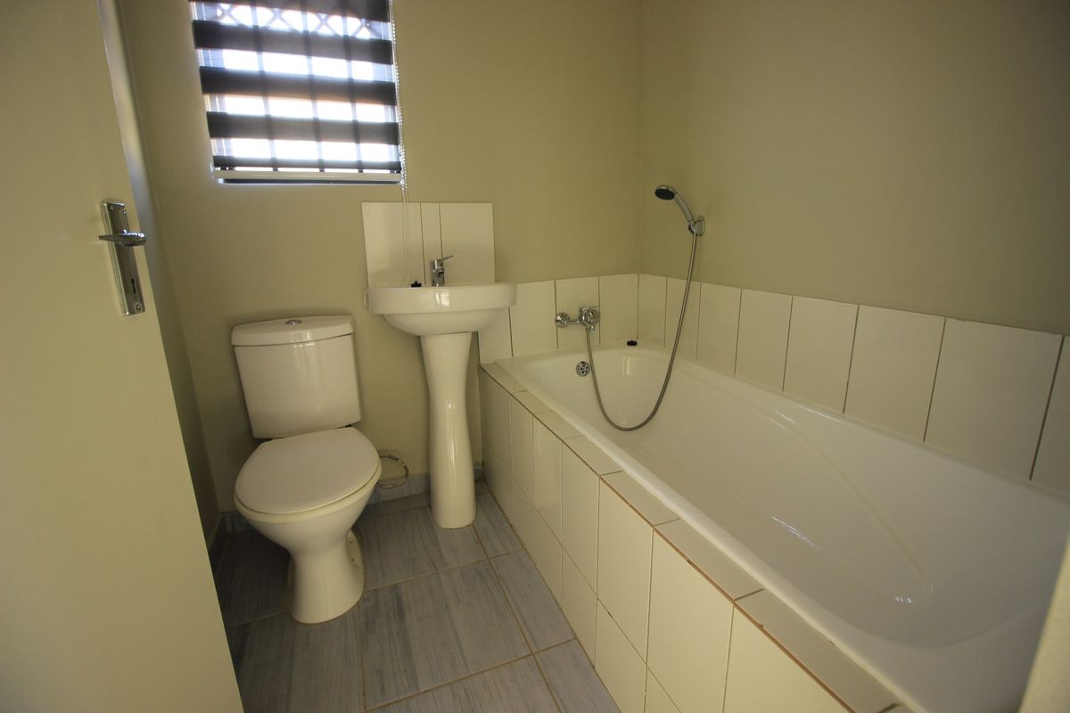A functional bathroom featuring a pedestal basin, toilet, and a bathtub with a shower mixer, finished with neutral wall paint and tiled flooring.
