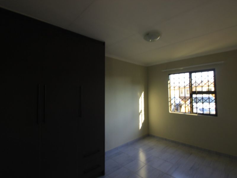 A vacant bedroom featuring tiled flooring, a built-in wardrobe, and a window fitted with a security gate.