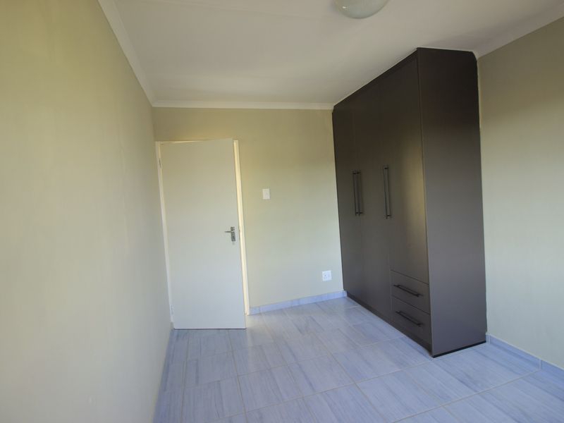A clean, empty bedroom featuring neutral wall paint, tiled flooring, and a modern dark-toned built-in wardrobe.