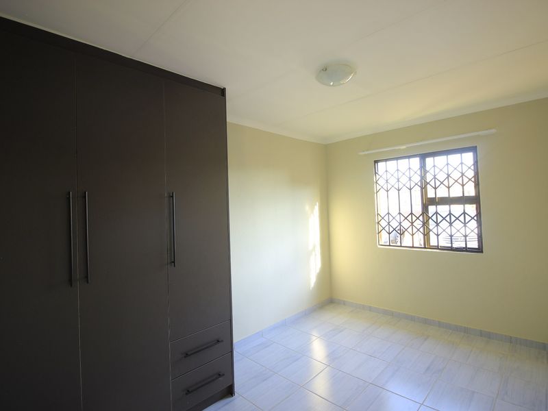 A clean, empty bedroom featuring neutral wall paint, tiled flooring, and a large dark-toned built-in wardrobe with modern handles.