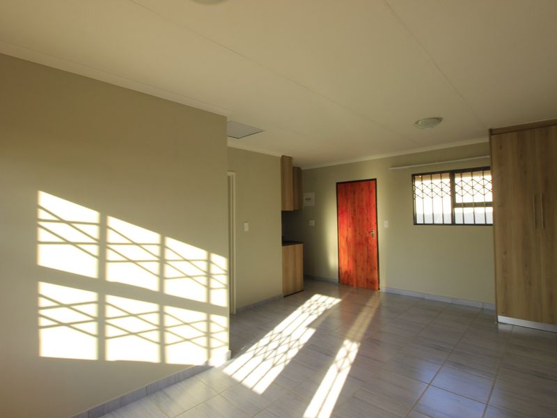 A bright, empty bedroom featuring tiled flooring, built-in cupboards, and security bars on the windows.