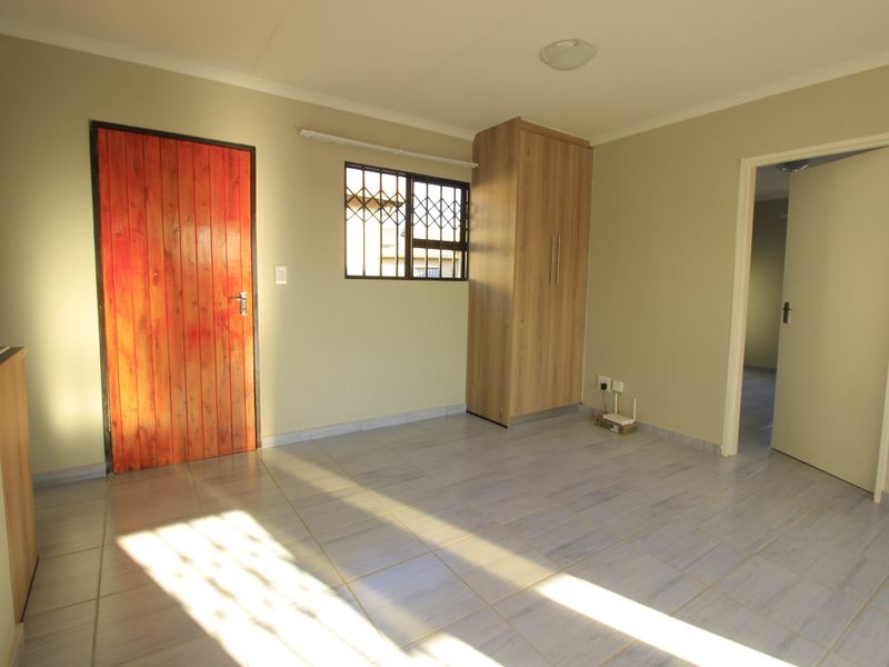 A clean, empty bedroom featuring tiled flooring, a built-in wardrobe, and a window fitted with security burglar bars.