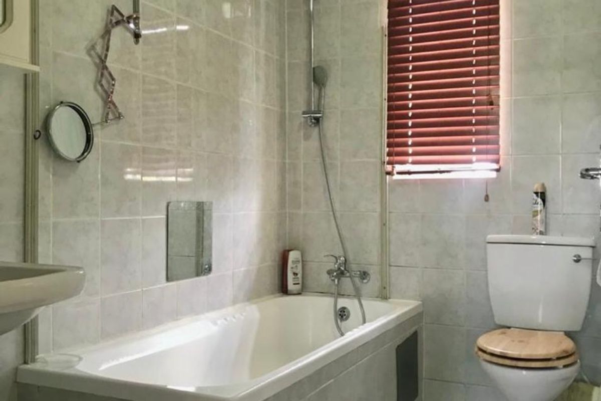 A functional bathroom featuring a built-in bathtub with shower mixer, toilet, and basin, finished with neutral wall and floor tiling.