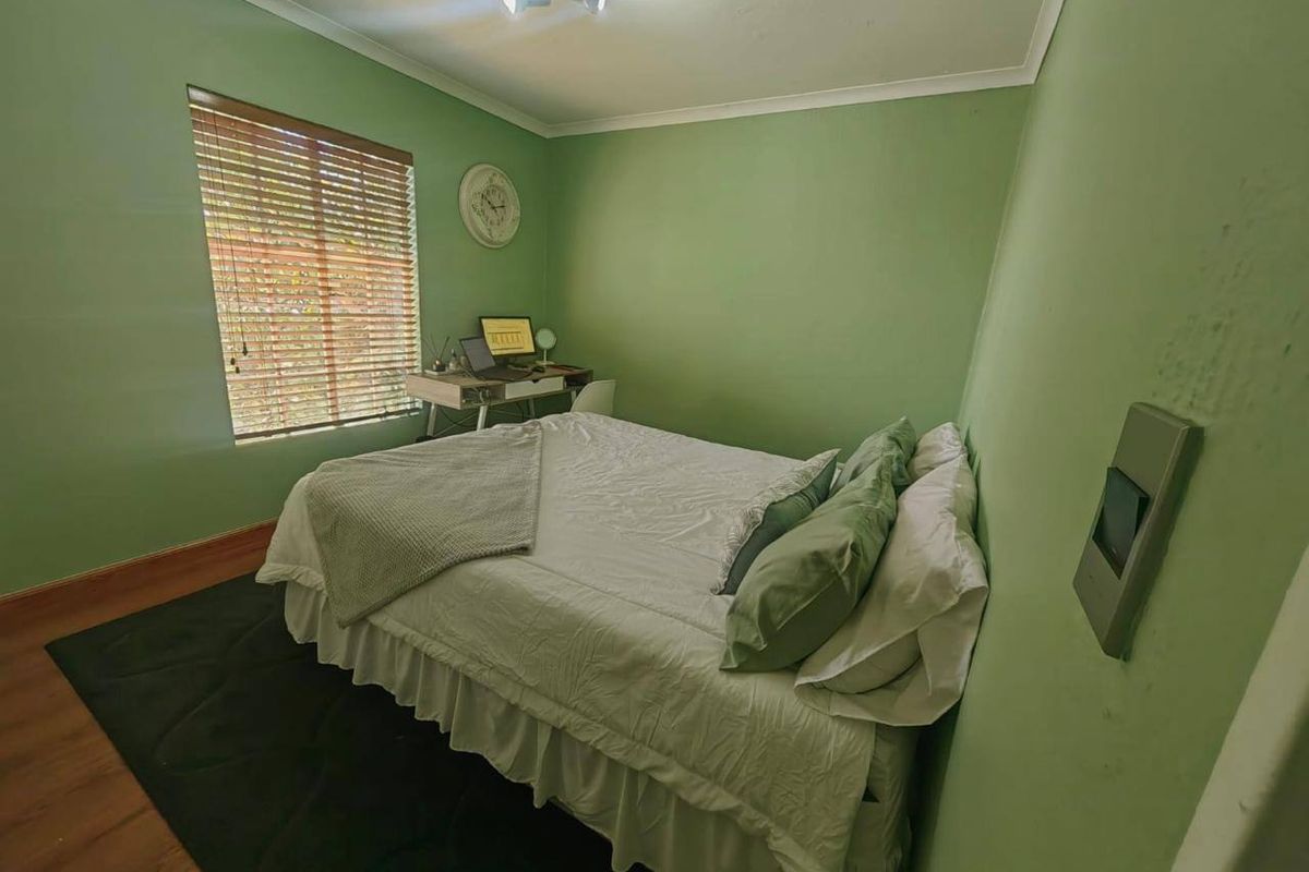 A functional bedroom featuring laminate flooring, cove cornicing, and a window fitted with venetian blinds, providing a comfortable and well-lit living space.