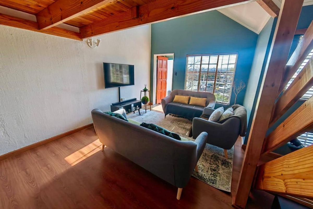 Bright living room featuring exposed timber ceiling beams, laminate flooring, and a staircase, creating a warm and inviting atmosphere.