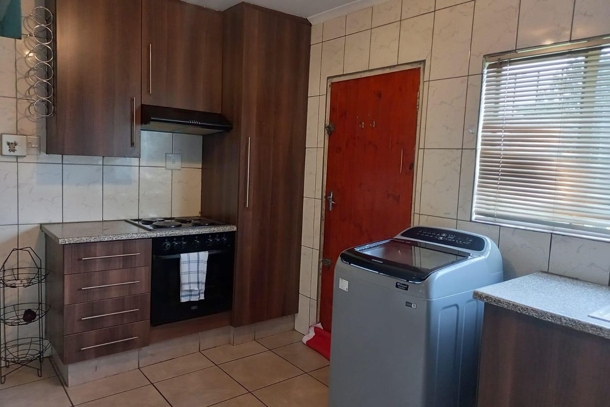 Functional kitchen featuring dark wood cabinetry, built-in oven and hob, tiled splashbacks, and tiled flooring with direct access to an exterior door.