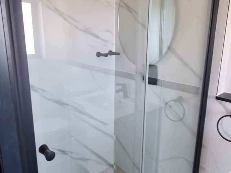 A modern bathroom featuring a glass shower enclosure with black framing and elegant marble-look wall tiles.