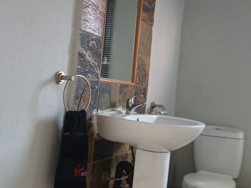 A functional bathroom featuring a pedestal basin with a slate tile splashback, a standard toilet, and a window with a venetian blind.